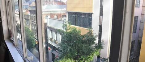 A view from a window overlooking a cityscape with modern and historic buildings, a tree, and a street.