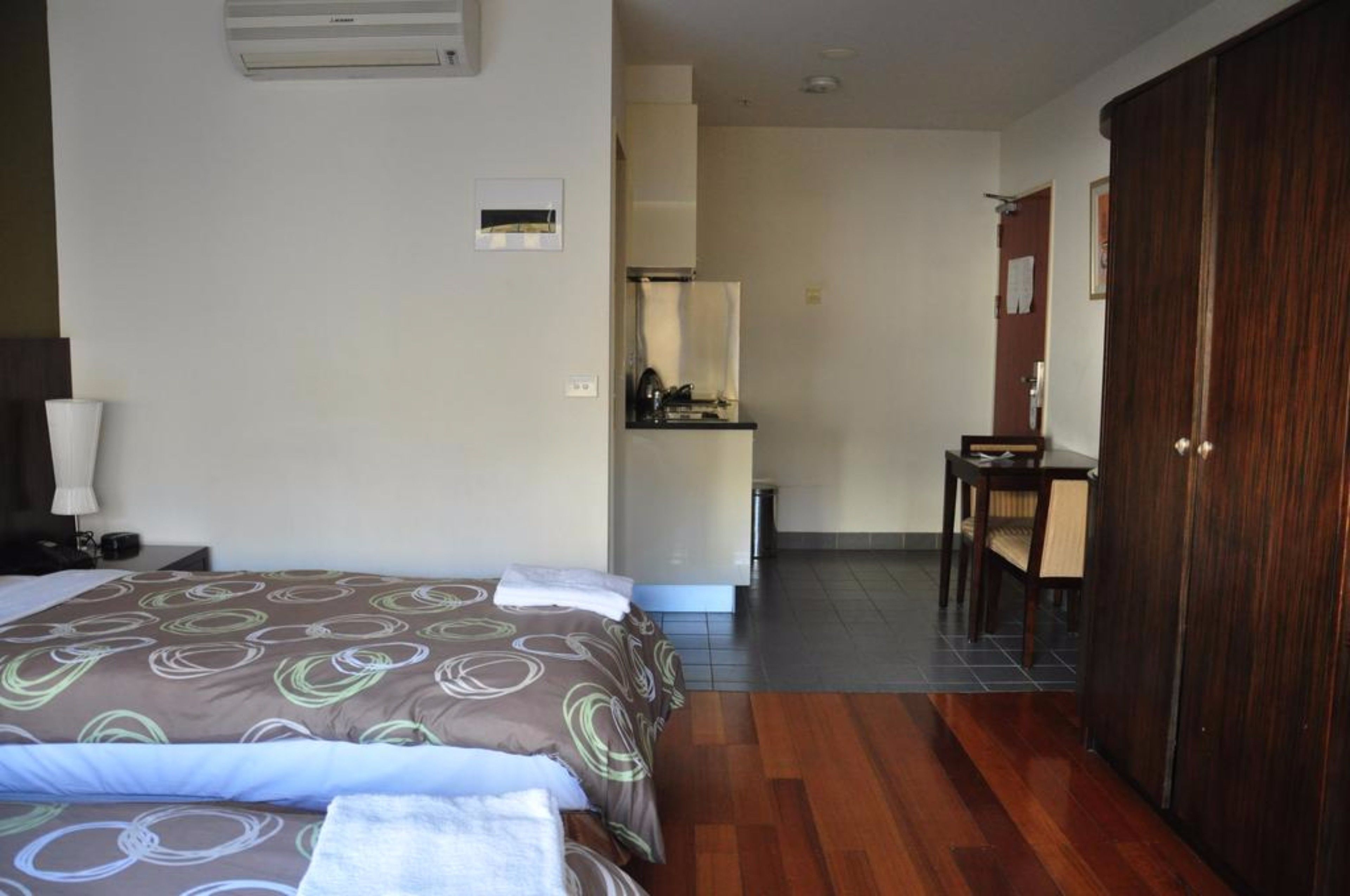 A hotel room with a bed, a desk, a chair, a wardrobe, and a bathroom visible through an open door.