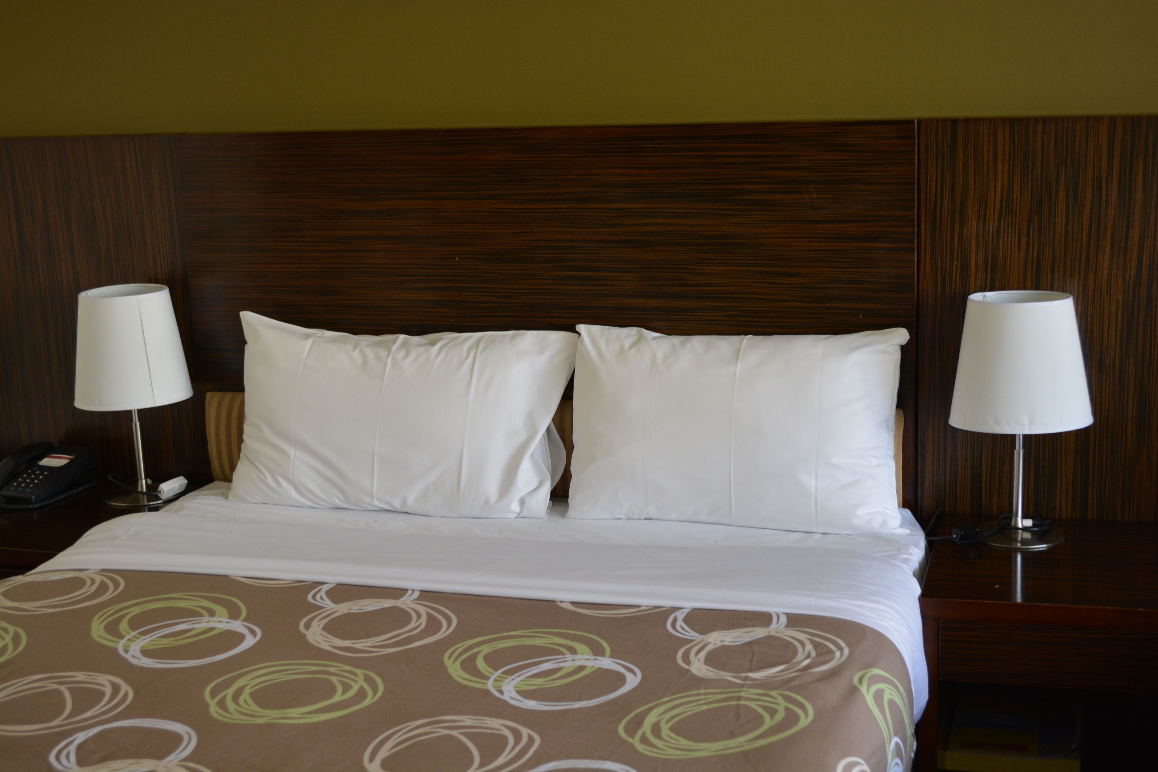 Habitación de hotel con una cama grande, dos lámparas de noche, un teléfono y una colcha estampada.