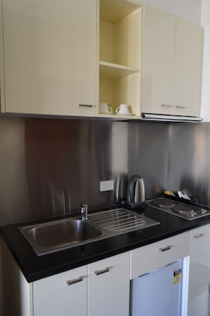 A kitchen with a stainless steel sink, a kettle, and a refrigerator.