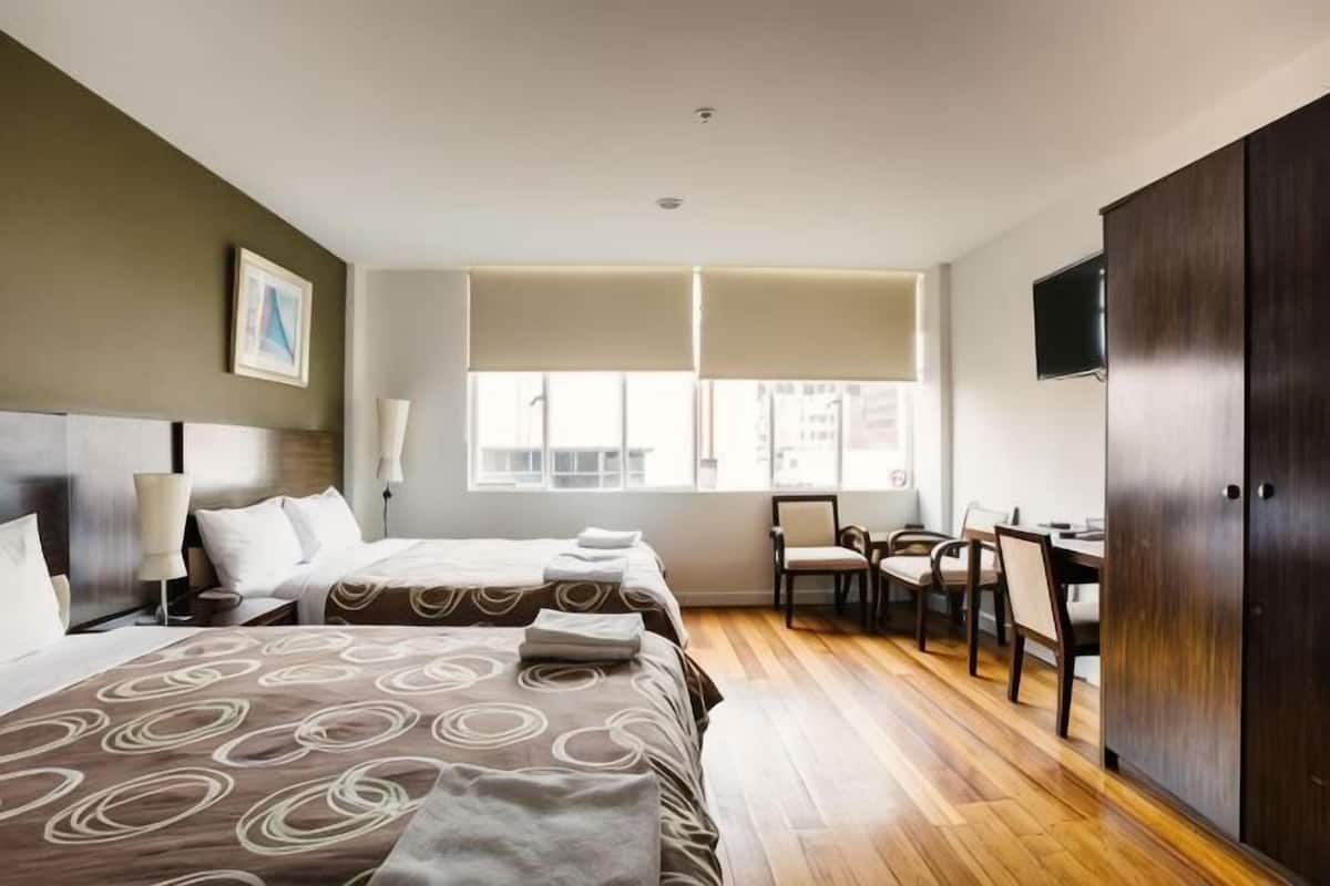 Habitación de hotel con dos camas, un escritorio, una silla, un televisor y un armario.