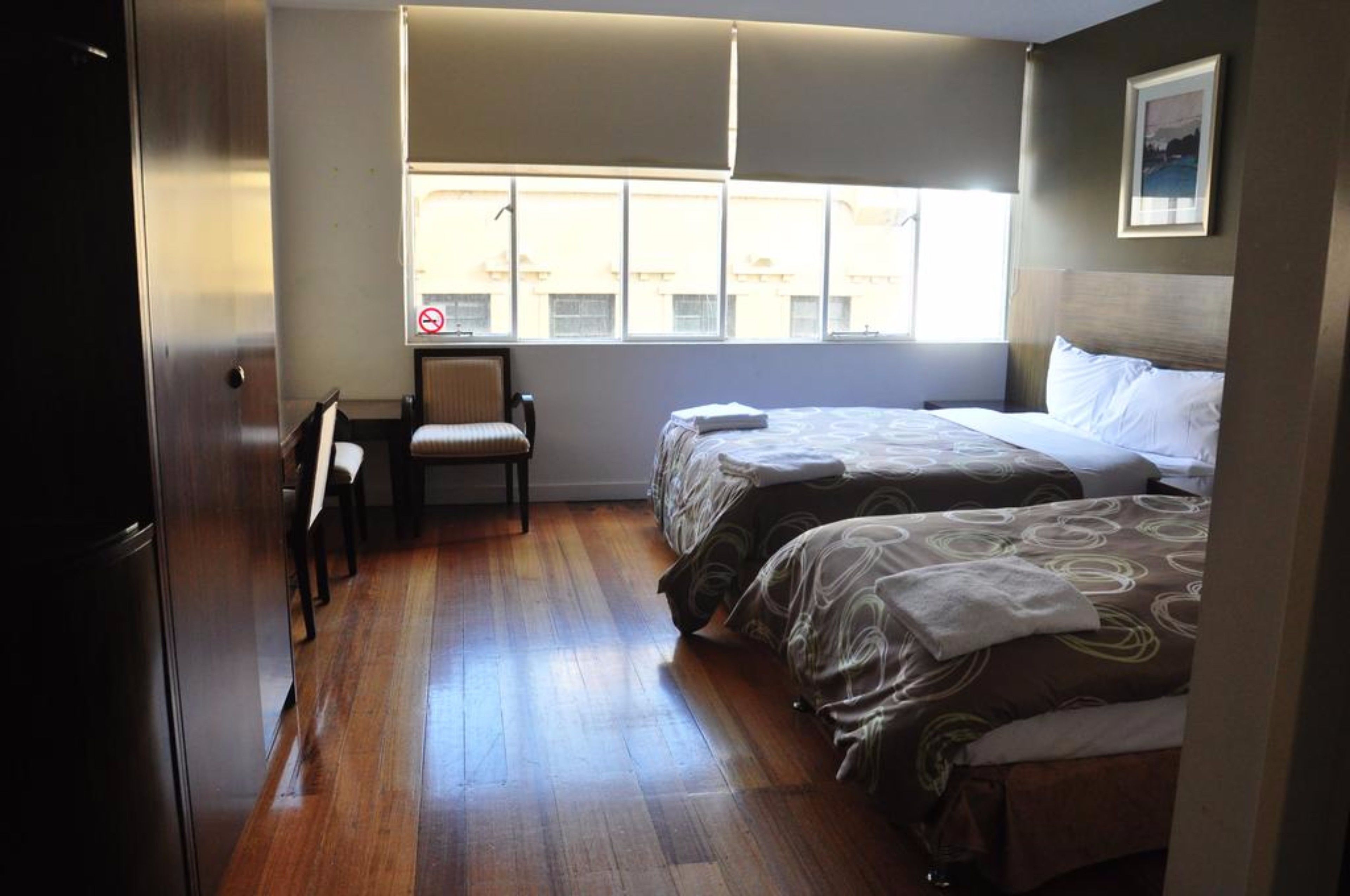 Habitación de hotel con dos camas, una silla, una ventana que ofrece vistas a edificios y una puerta.