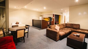 A modern living room with a brown sectional sofa, a red couch, a wooden coffee table, and a dining area with a round table and chairs. - YTI Garden Hotel (Melbourne)