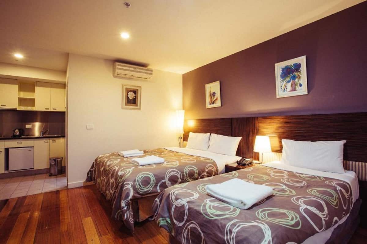 Una habitación de hotel con dos camas, kitchenette y obras de arte en las paredes.