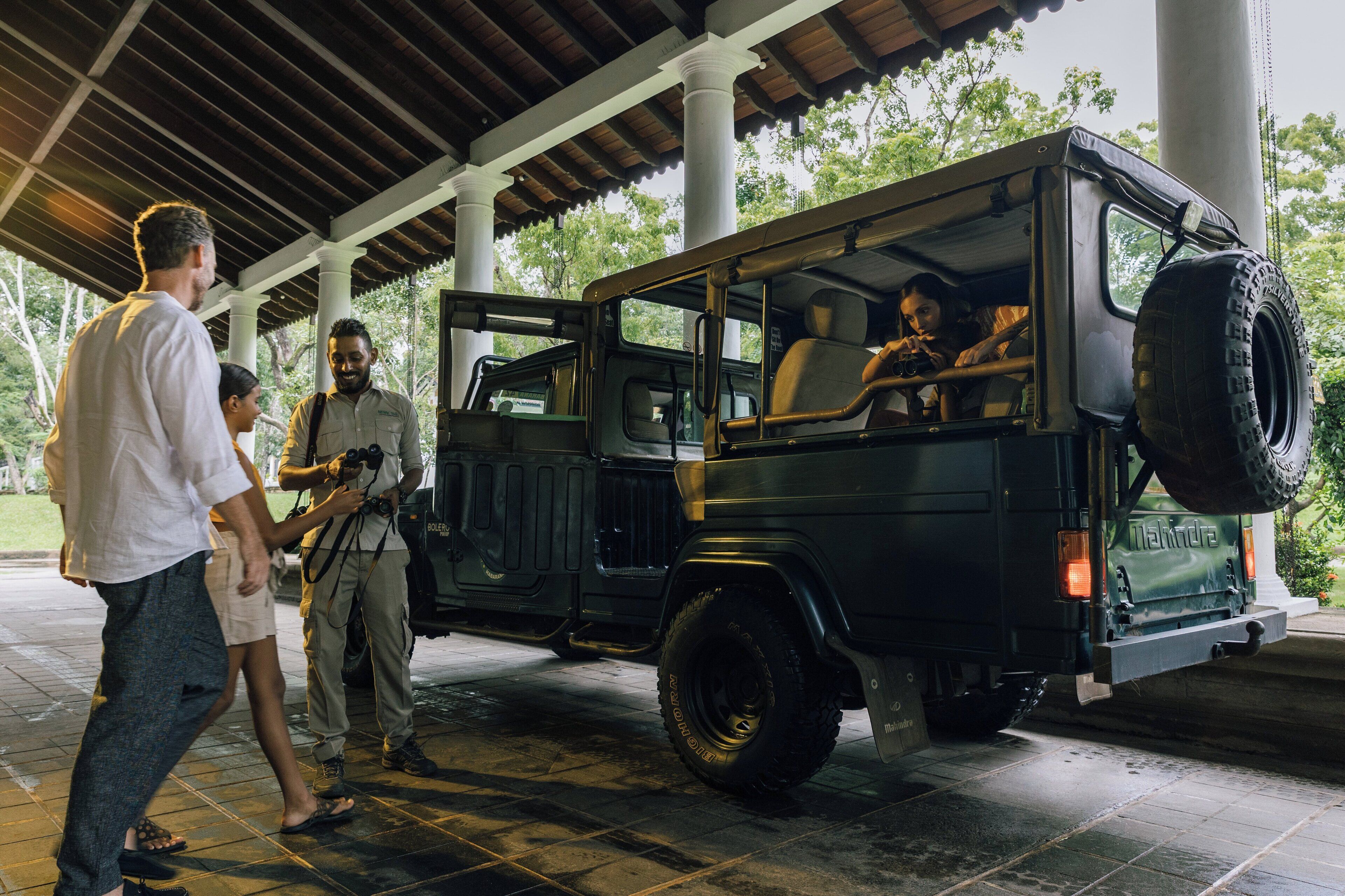 A black jeep with a spare tire mounted on the back, parked under a covered area with white columns.