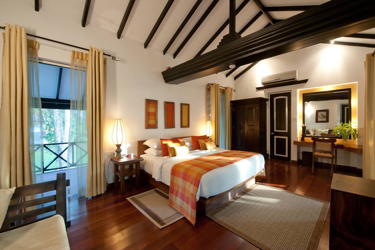 A bedroom with a large bed, wooden beams, a desk, and a mirror.