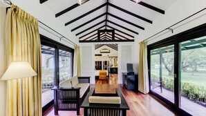 Une pièce spacieuse avec un plafond haut, des poutres en bois, un canapé, une table et de grandes fenêtres donnant sur l’extérieur.