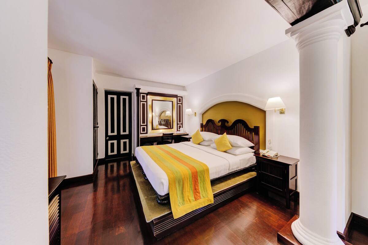 A hotel room with a large bed, a wooden headboard, a nightstand, and a bedside table.