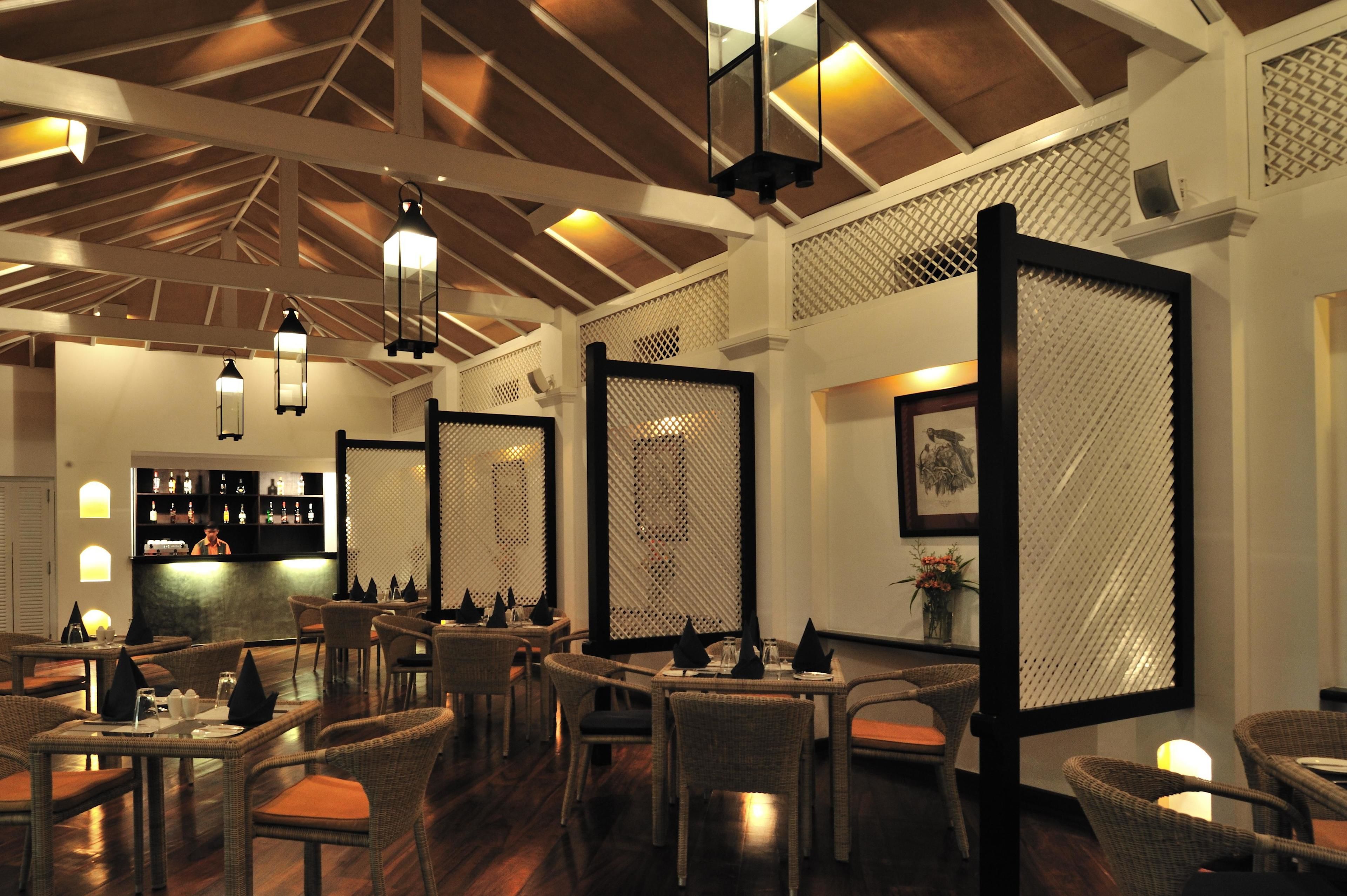 A restaurant with wicker chairs, tables, and hanging lanterns.