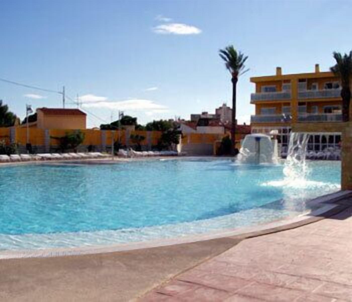 A swimming pool with a water fountain, surrounded by buildings with balconies.