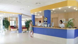 A reception area with a blue counter, two receptionists, and a waiting area with chairs and plants. - Terralta (Benidorm)