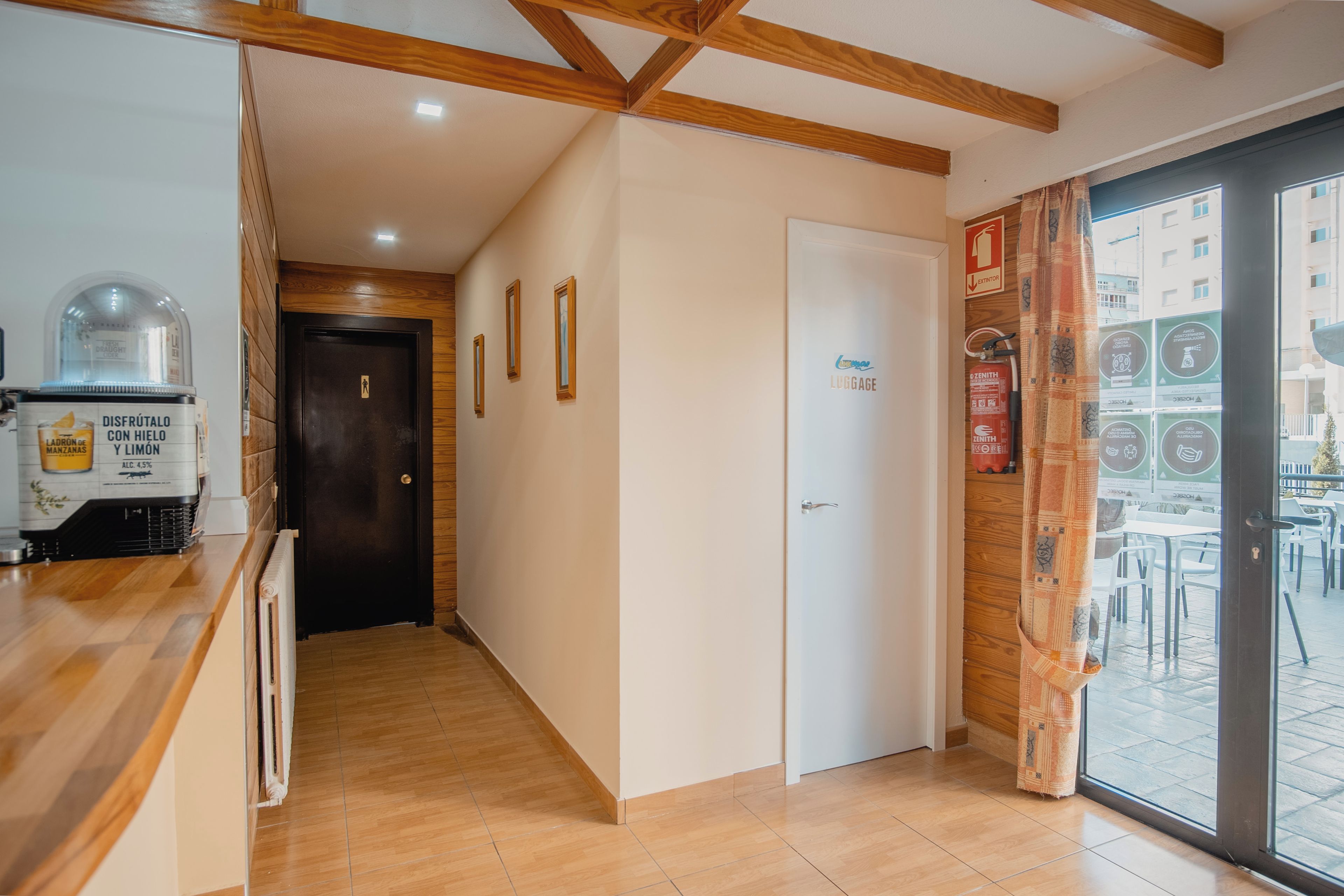 A hotel corridor with a wooden floor, a reception desk, a door with a sign, and a window with a view of buildings.