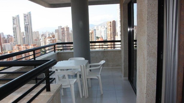Un balcón con mesa y sillas, barandilla y vista a la ciudad.