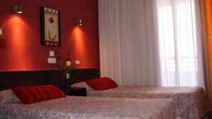 A hotel room with two beds, a red wall, a framed picture, and a window with curtains.