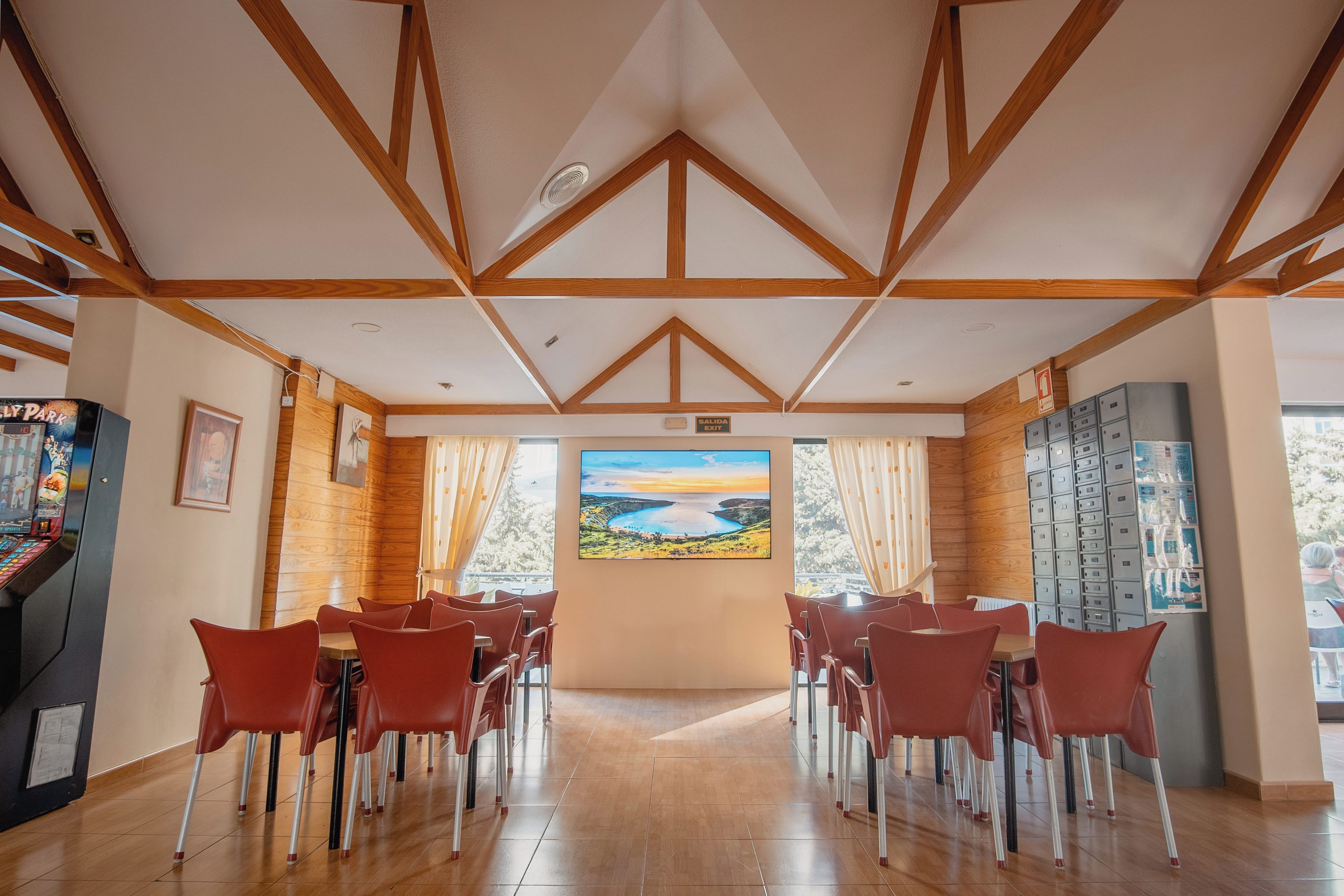 Una habitación con techo de madera, un cuadro de un paisaje, sillas rojas y vistas al exterior.