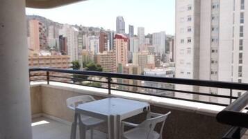 A balcony with a table and chairs, overlooking a cityscape with high-rise buildings.