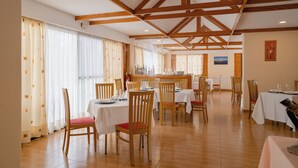Un amplio comedor con vigas de madera en el techo, mesas blancas y sillas con cojines rojos.