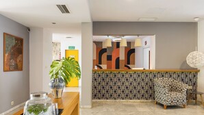 A reception area with a wooden counter, a potted plant, and a patterned wall. - Colectia Hotel Santa Lucia (Seville)