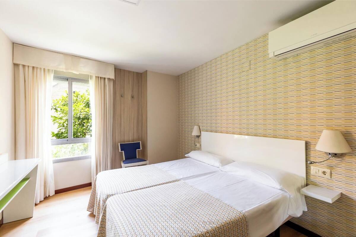 A hotel room with a bed, a desk, a chair, and a window with curtains.
