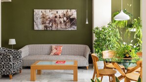 A living room with a sofa, coffee table, and chairs, a painting on the wall, and a large potted plant. - Colectia Hotel Santa Lucia (Seville)