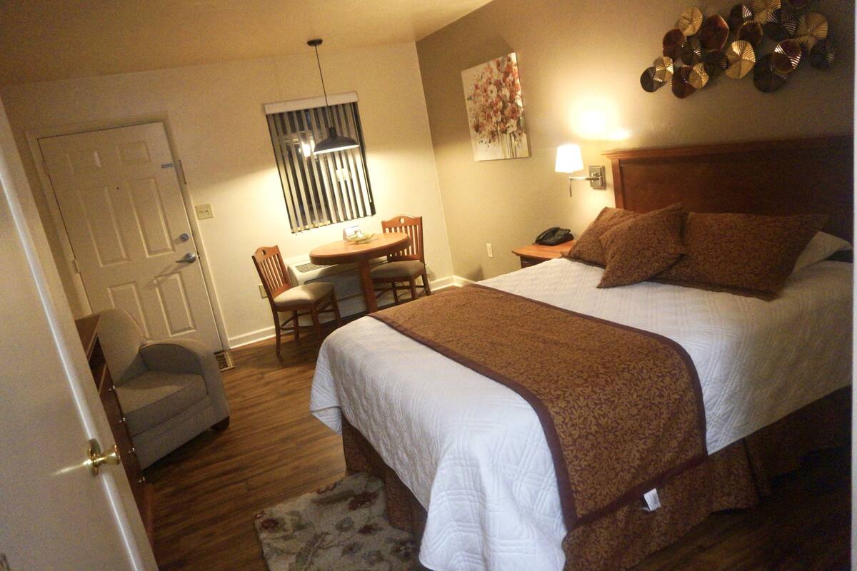 A hotel room with a bed, a desk, a chair, and a lamp.