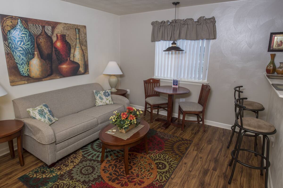 A living room with a sofa, coffee table, and chairs, a dining area with a table and chairs, and a large painting on the wall.