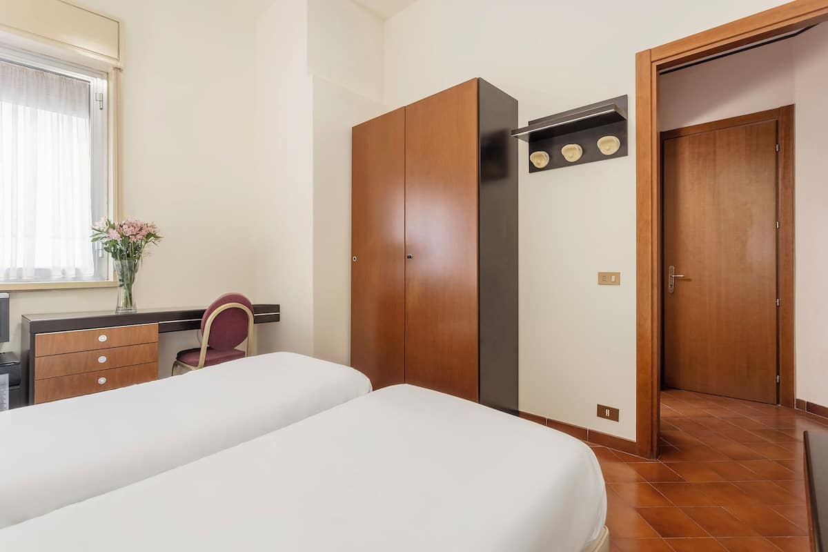 A bedroom with two beds, a desk with a chair, a wardrobe, and a bathroom door.