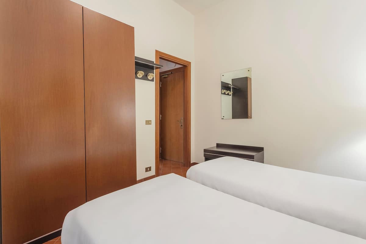 A hotel room with two beds, a wooden wardrobe, a small desk, and a mirror on the wall.