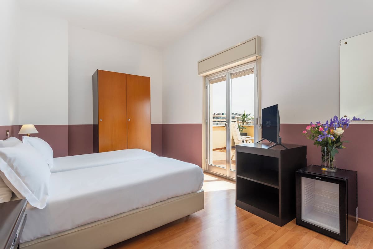 A hotel room with a bed, a TV, a small black cabinet, and a mirror on the wall.