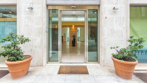 The entrance to Hotel Europa with a clear glass facade, a reception area visible inside, and two potted plants on either side. - Crisol Europa (Palermo)