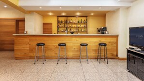 A bar area with a wooden counter, three stools, and a TV screen displaying 'CRISOLO HOTELS'. - Crisol Europa (Palermo)