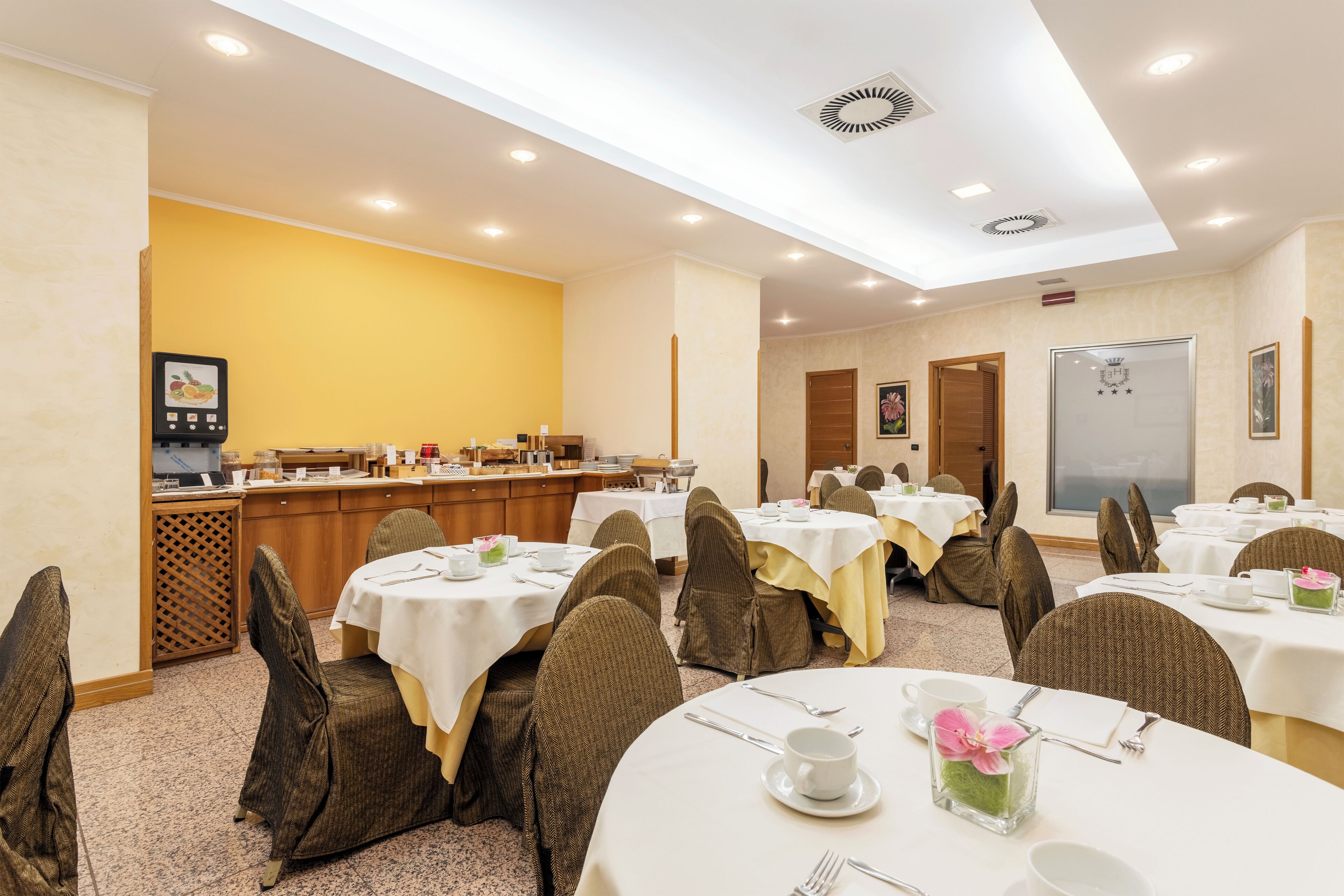 A hotel dining area with round tables, chairs, and a buffet counter.