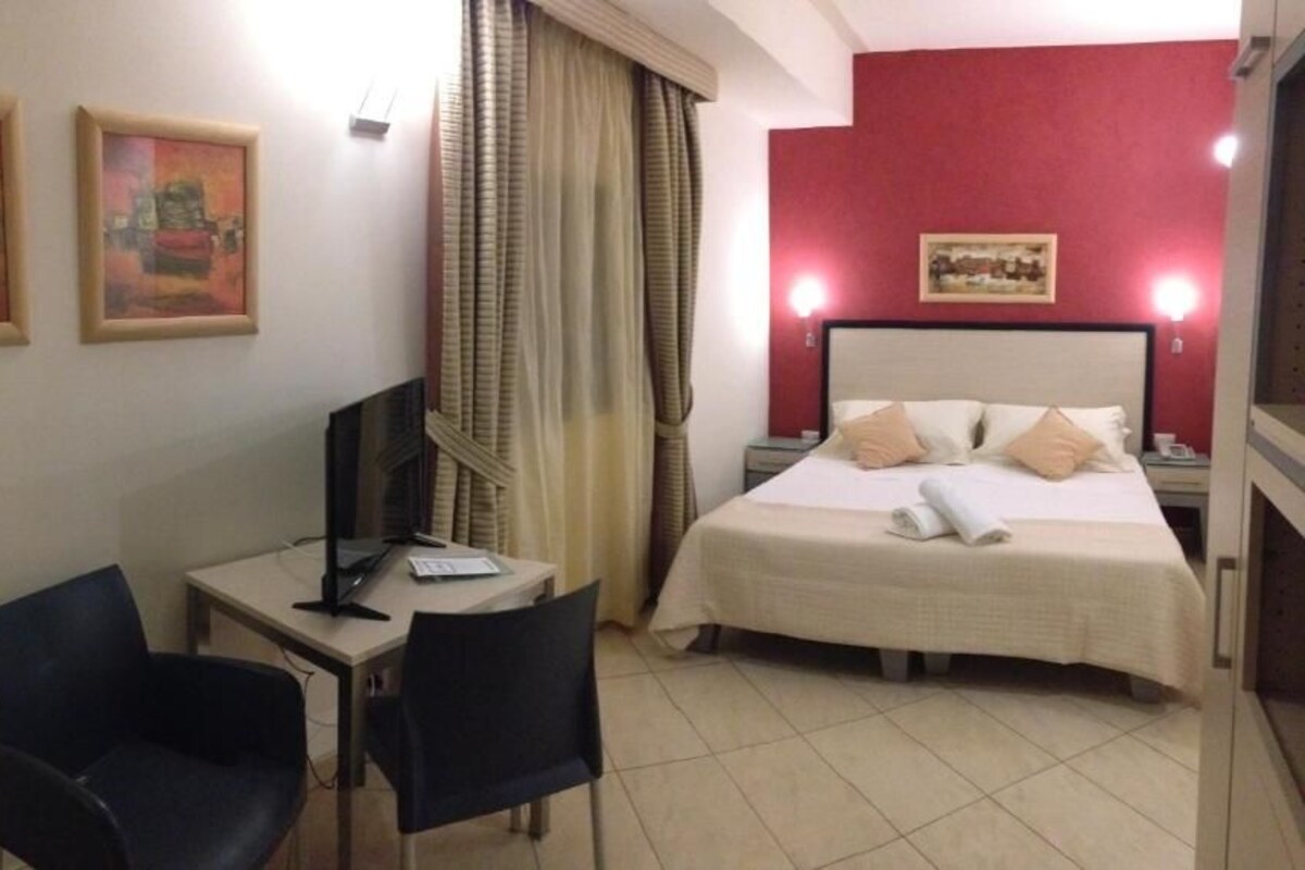 A hotel room with a bed, a desk, two chairs, a TV, and artwork on the walls.