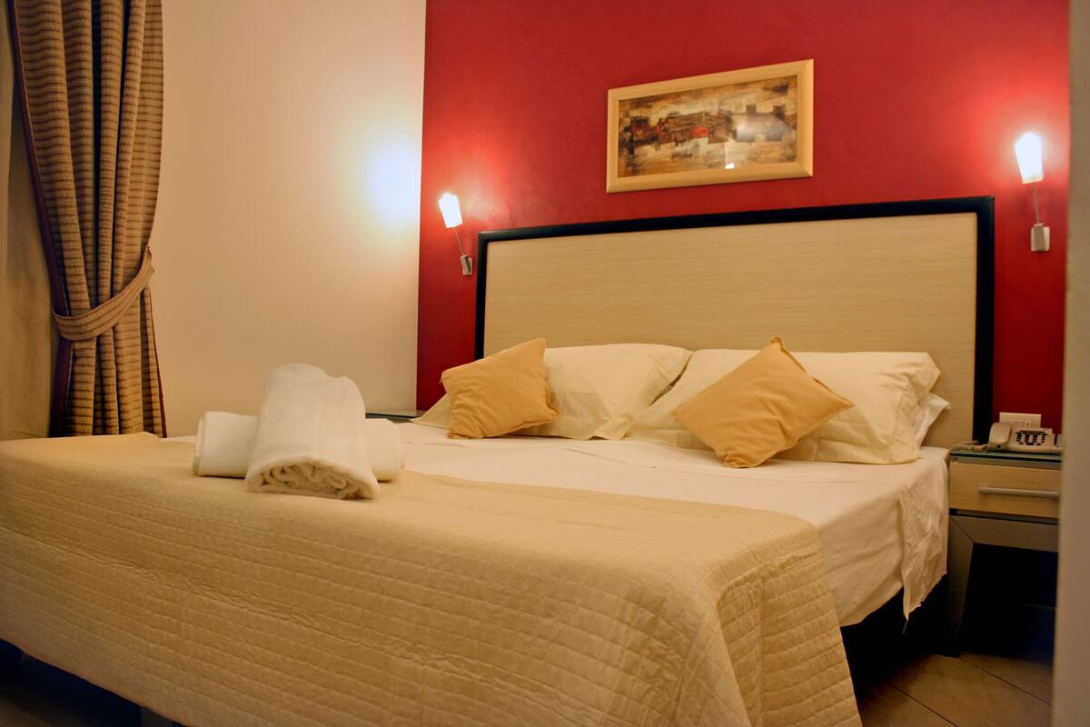 Una habitación de hotel con una cama, una mesita de noche, un teléfono y un cuadro en la pared.