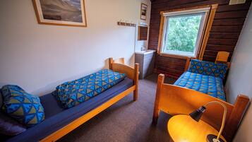 A small, compact room with two single beds, a bedside table with a lamp, a small window, and a wall-mounted mirror.