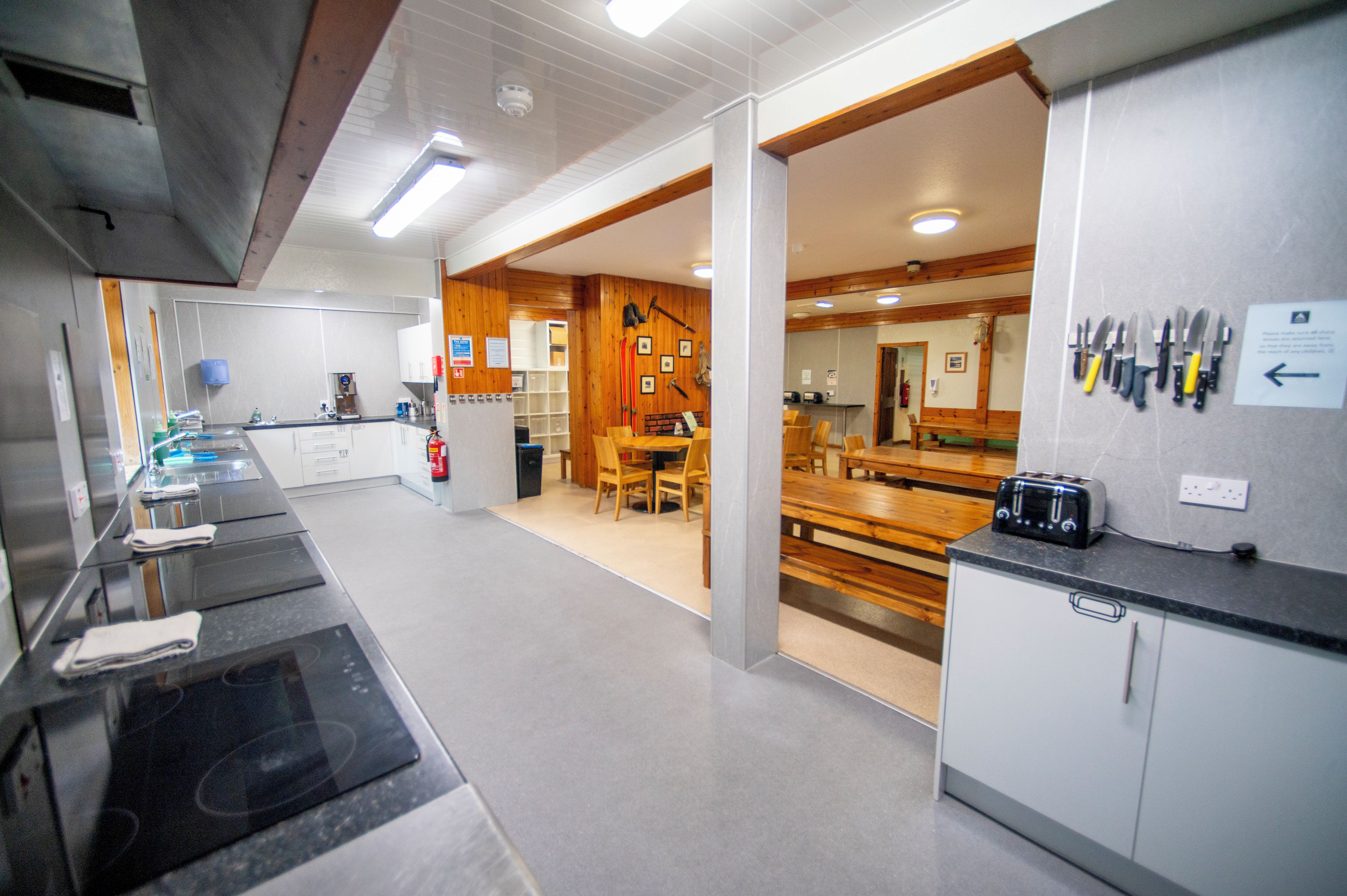 Una cocina moderna con una isla central, detalles de madera y un comedor con mesas y sillas de madera.