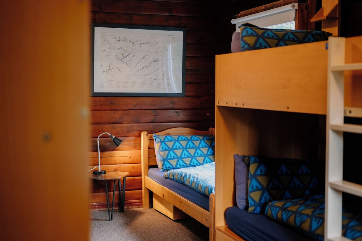 A cabin interior with a bunk bed, a desk with a lamp, and a map on the wall.