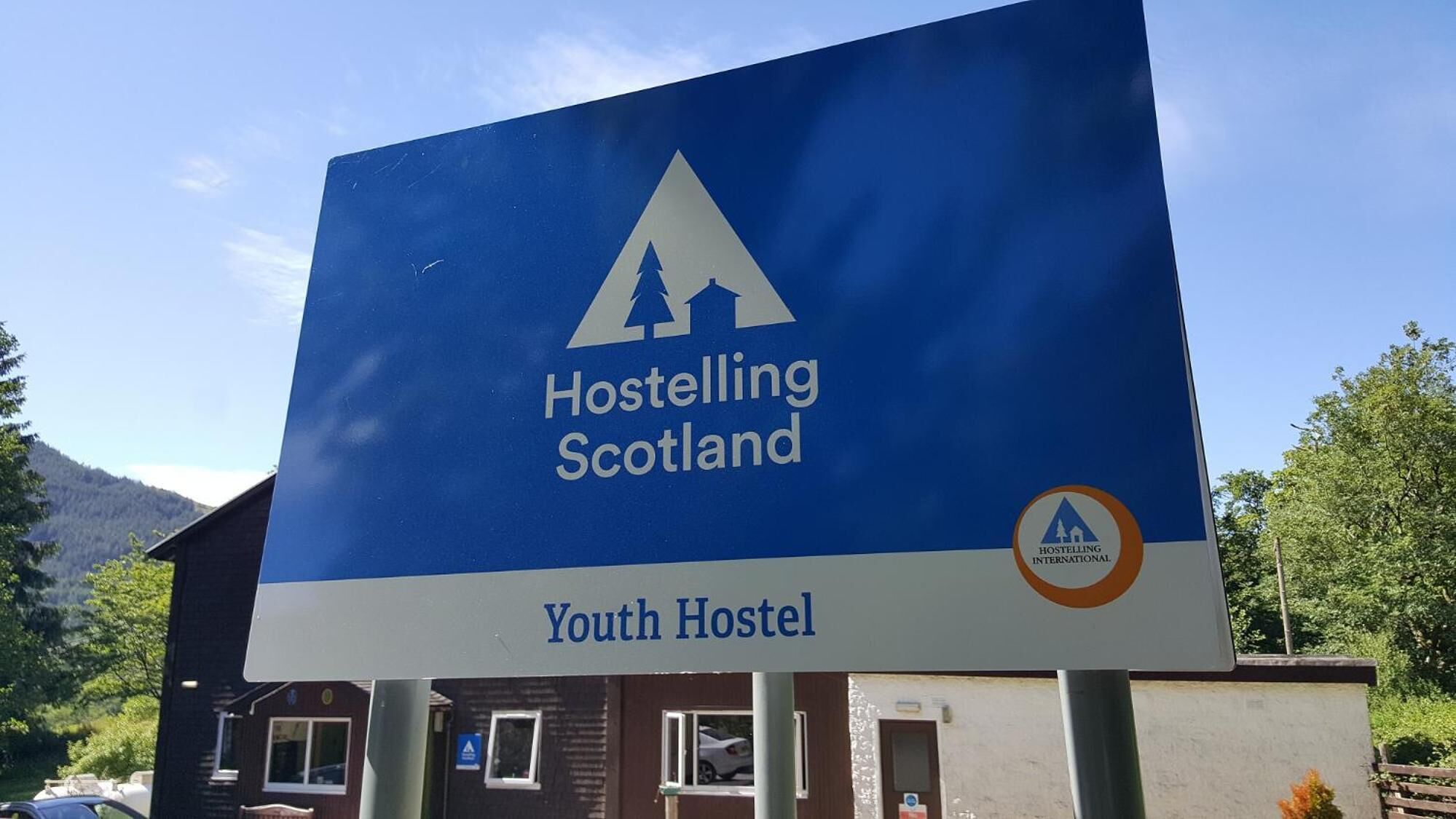 A large blue sign advertising Hostelling Scotland with a mountain and tent icon, and the text "Youth Hostel" below.