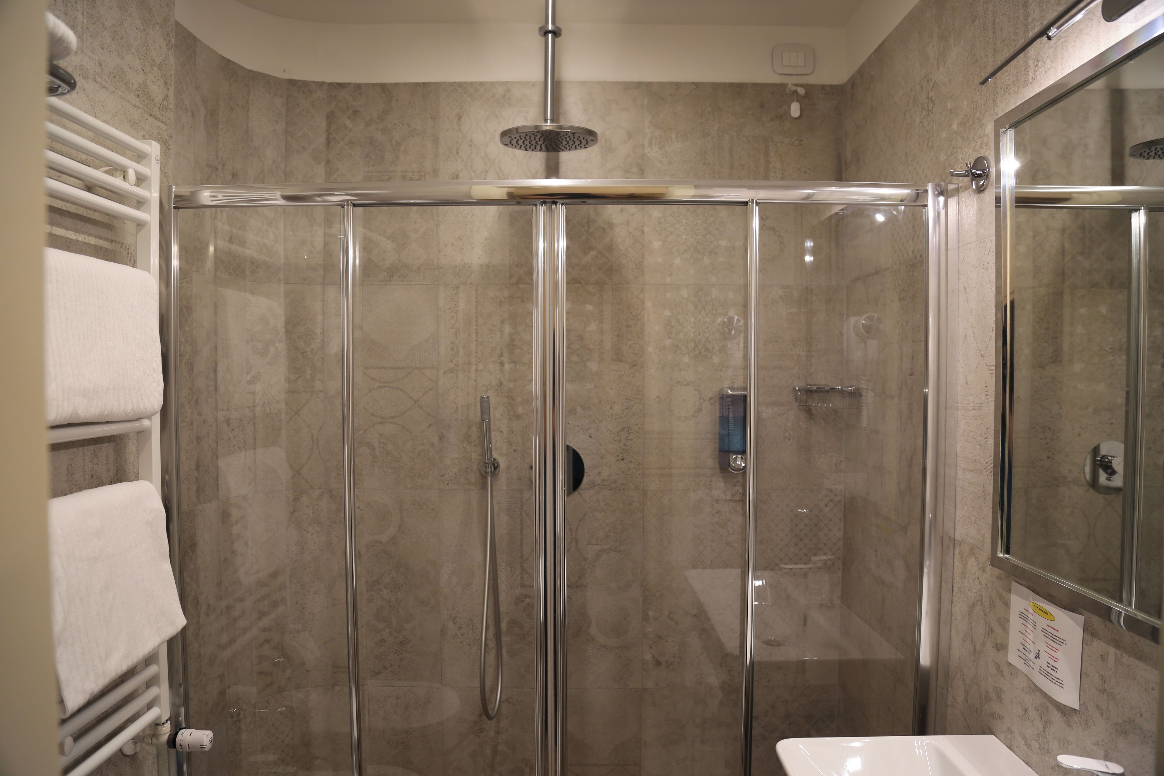 A glass-enclosed shower stall with a handheld showerhead, a wall-mounted towel rack, and a sink with a mirror.