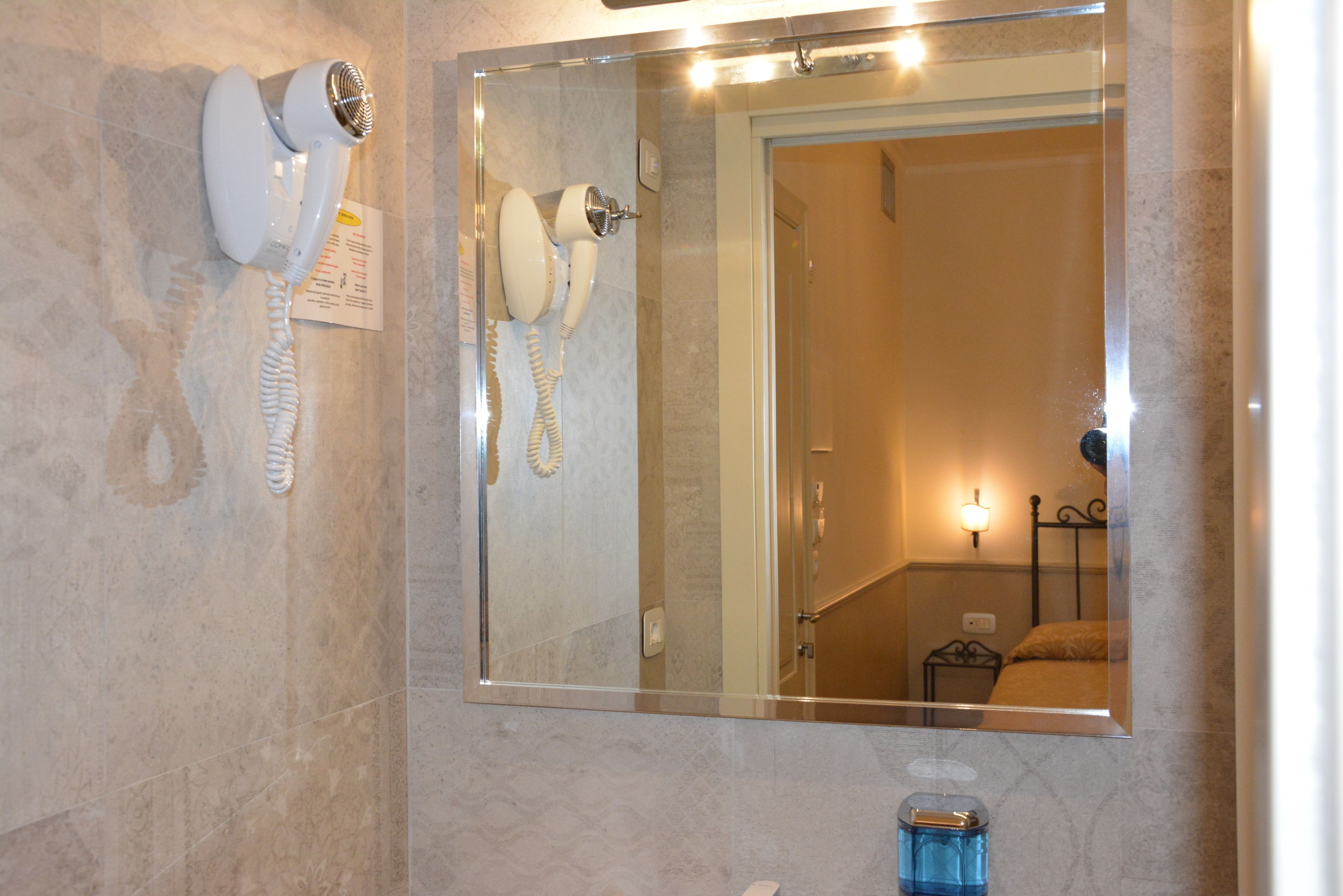 A bathroom with a hairdryer mounted on the wall, a mirror, and a sink with a blue soap dispenser.