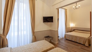 Una habitación de hotel con dos camas, un televisor montado en la pared, suelo de madera y un candelabro.