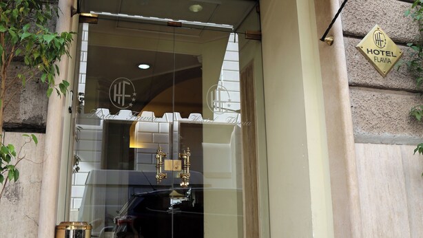 Una entrada de hotel con puerta de cristal, alfombra roja y placa dorada.
