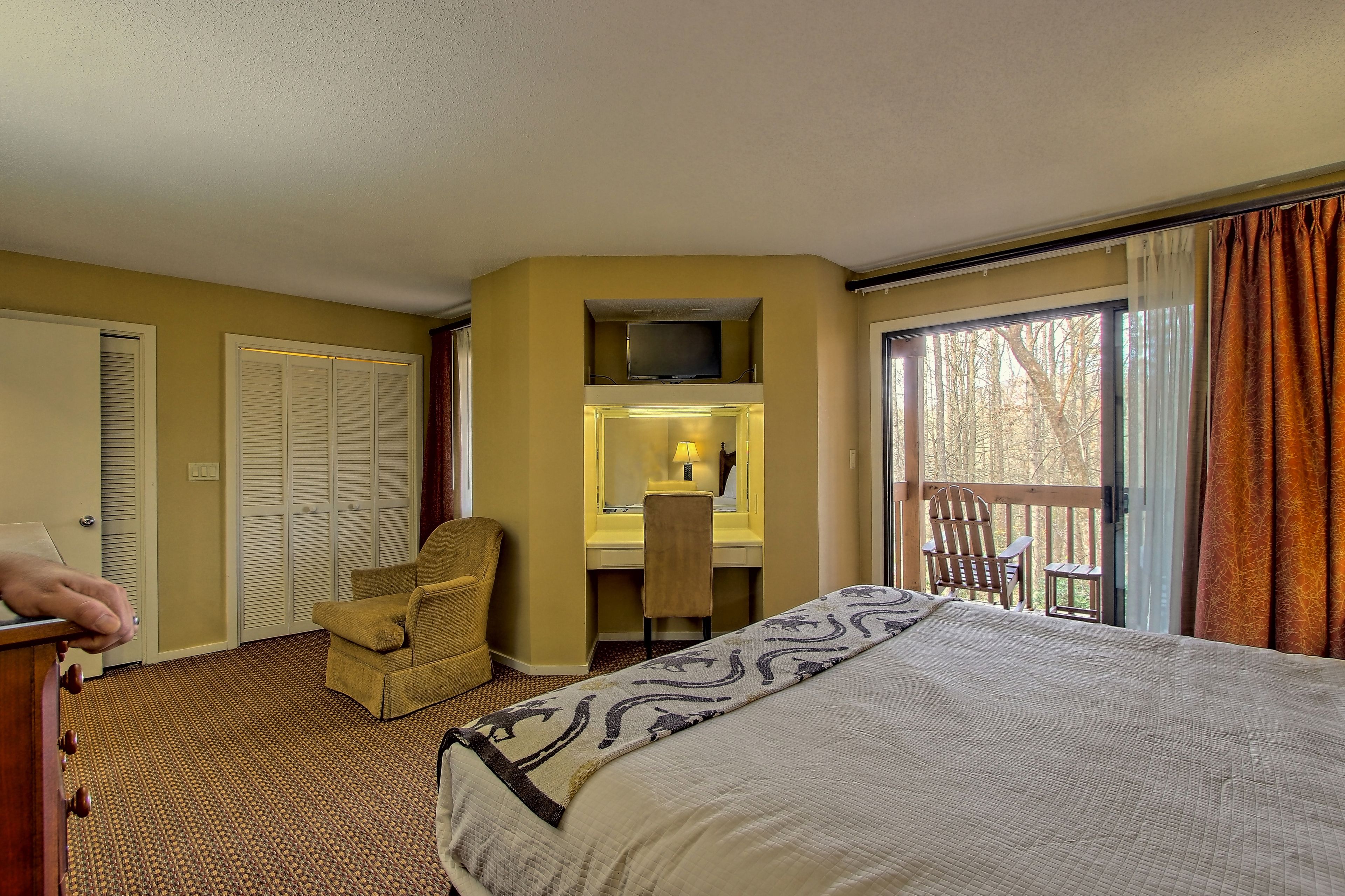 A hotel room with a bed, a desk with a chair, a TV, and a balcony with curtains.