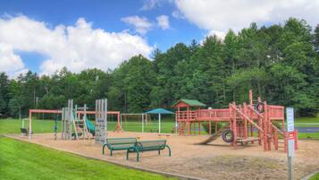 Explore the playground area with a slide, swings, and climbing frames, surrounded by a grassy lawn and shaded seating.