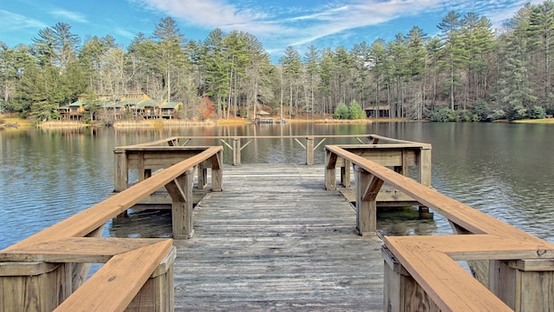 A wooden pier leading to a dock with benches, surrounded by a forest and a lake. - Foxhunt at Sapphire Valley (Sapphire)