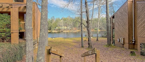 Una cabaña de madera con una escalera que lleva a una terraza con vistas a un lago, rodeada de árboles.