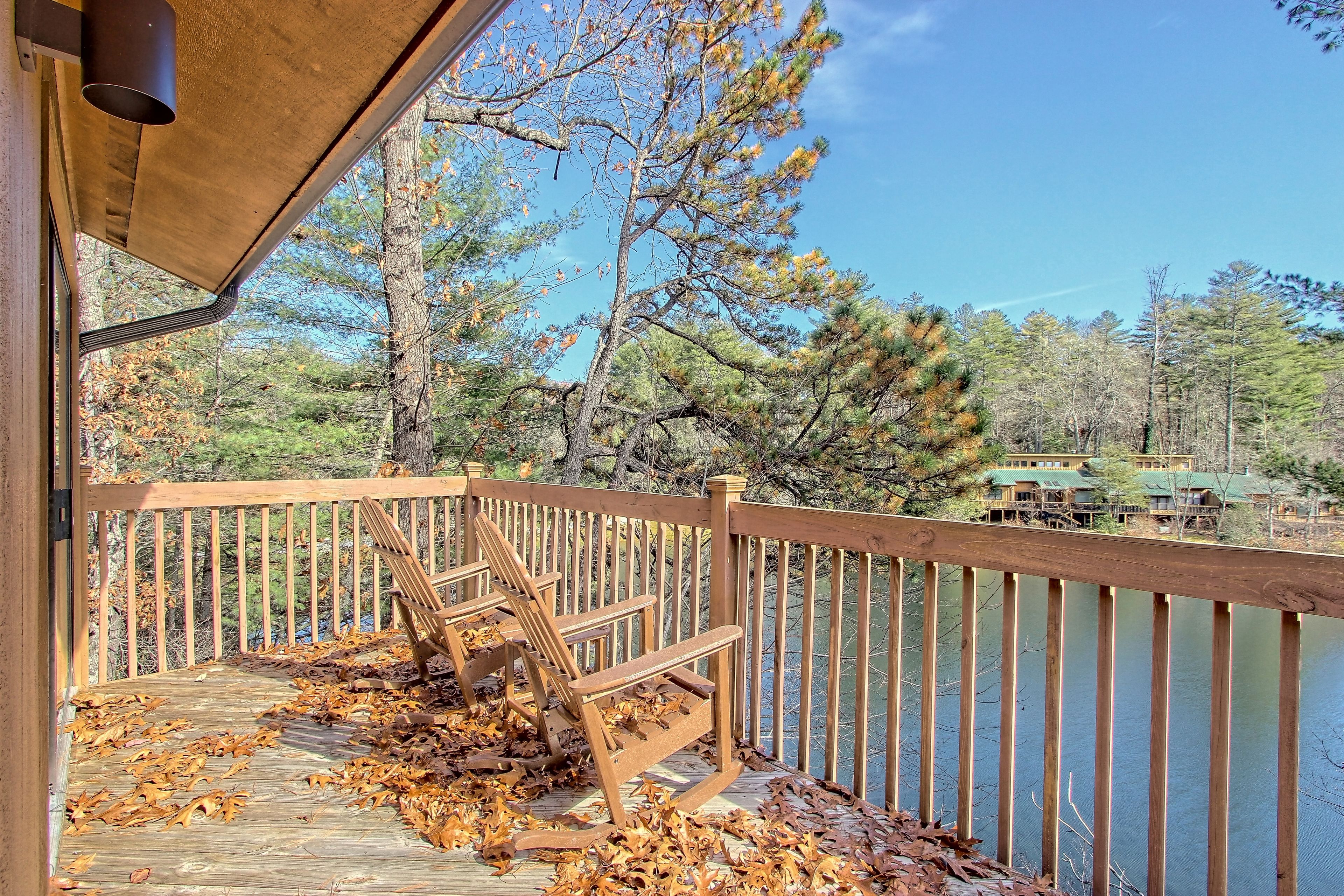 A wooden deck with a bench, surrounded by trees and a body of water.