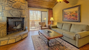 A cozy living room with a stone fireplace, a green sofa, a wooden ceiling fan, and a large painting on the wall. - Foxhunt at Sapphire Valley (Sapphire)