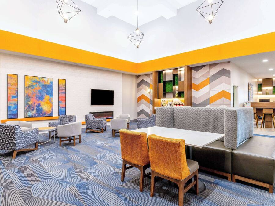 A modern hotel lobby with a central seating area, a flat-screen TV, and a bar area.