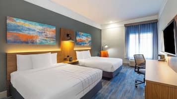 A hotel room with two beds, a desk, a TV, and artwork on the walls.